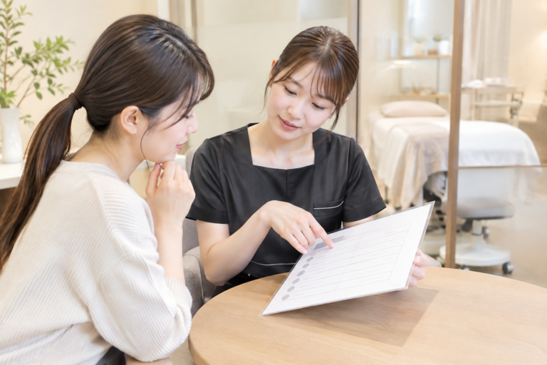サロン内で、女性スタッフが客に資料を見せながら説明している