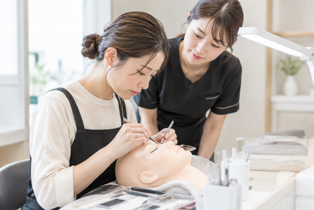 施術用ベッドで、研修中のスタッフが人形を使ってまつ毛の練習をしている様子