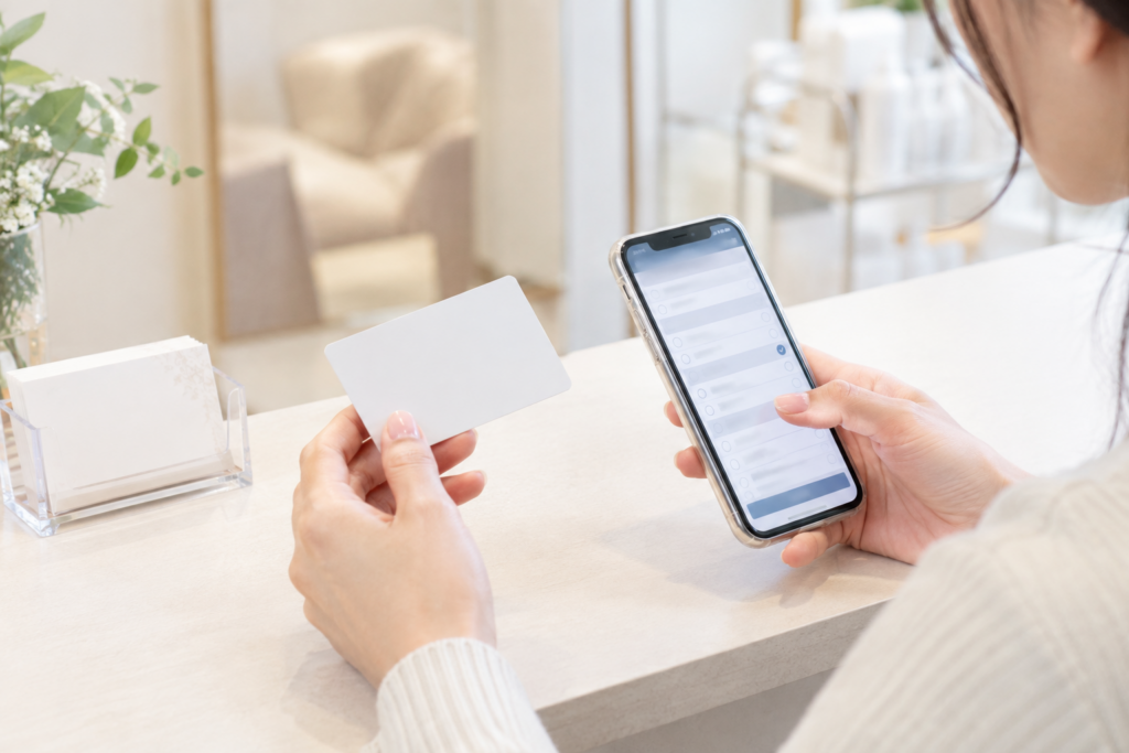 受付のような場所で、女性がスマートフォンを見ながらカードを確認している