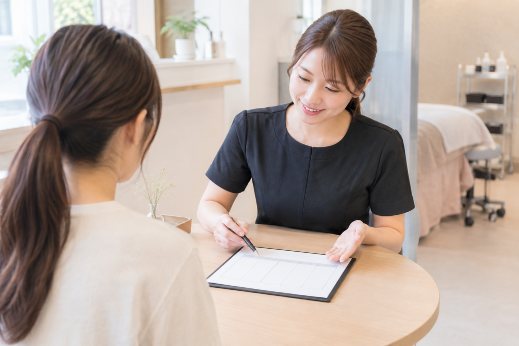 美容サロンで、スタッフが席に座る女性へ書類を見せながら説明している