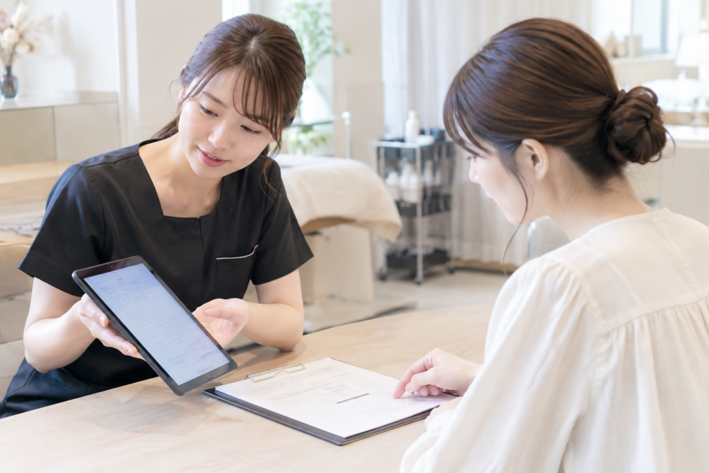 サロン内でスタッフがタブレットを見せながら説明し、女性が書類に目を通している
