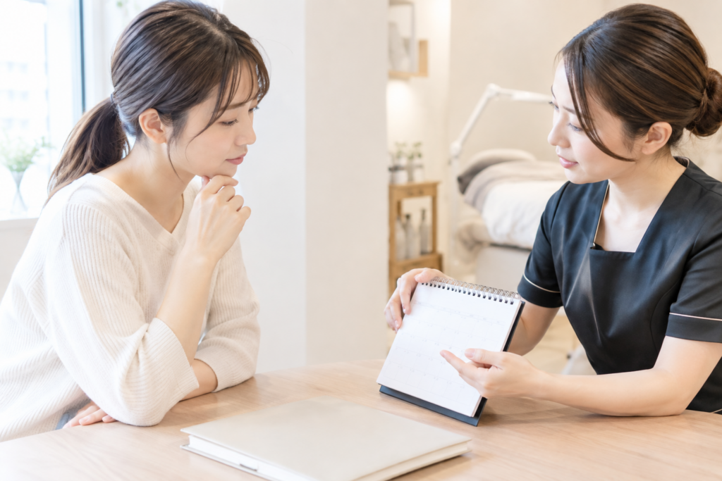 机を挟んで女性同士が面談し、相手がノートを見ながら説明している