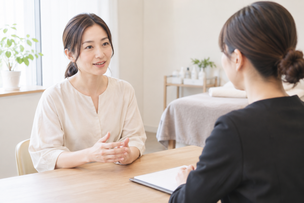 女性が席に座って面接官らしき相手と向かい合い、机越しに話している